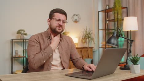 upset caucasian young man freelancer having sore throat while sitting at home office table desk