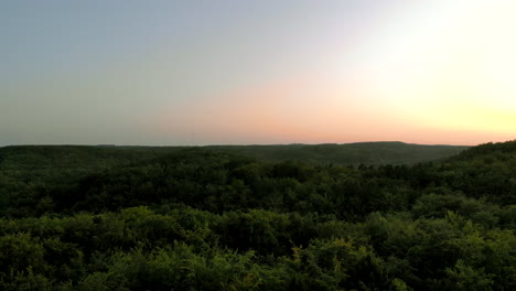 Imágenes-Aéreas-Sobre-El-Bosque-Durante-La-Puesta-De-Sol,-Hermoso-Cielo-En-El-Horizonte-Y-Coronas-De-árboles-Verdes-Debajo,-Paisaje-Natural-En-La-Ciudad,-Cerca-De-Edificios-Residenciales