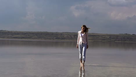 alone young woman in casual is walking on shallow of lake at summer