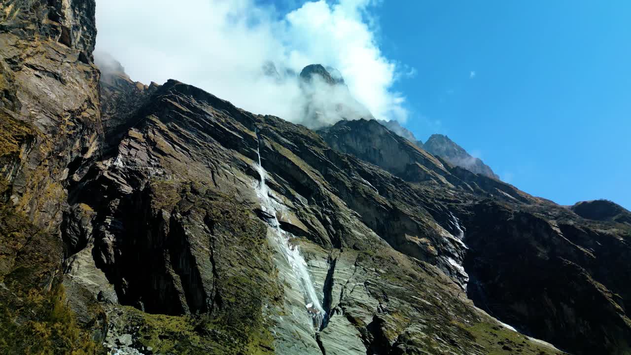 Tatopani waterfall flowing down a steep rocky mountain slope under clear blue sky surrounded by rugged terrain and misty air showing raw natural beauty of highlands Outdoors