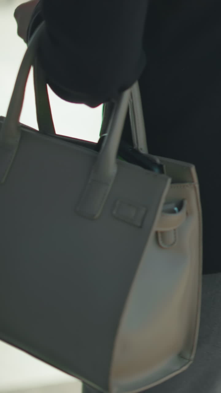 Side view of lady carrying ash handbag walking to office, about to open glass door, dressed in black jacket, professional setting, urban background blurred