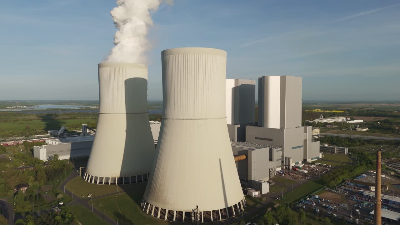Drone footage of the Lippendorf power station near Leipzig, Germany. Massive cooling towers release steam into the clear blue sky on a spring day.