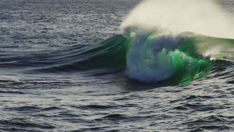 deep ocean wave crashes in from left, foamy crest and blue depths lit by late afternoon glow
