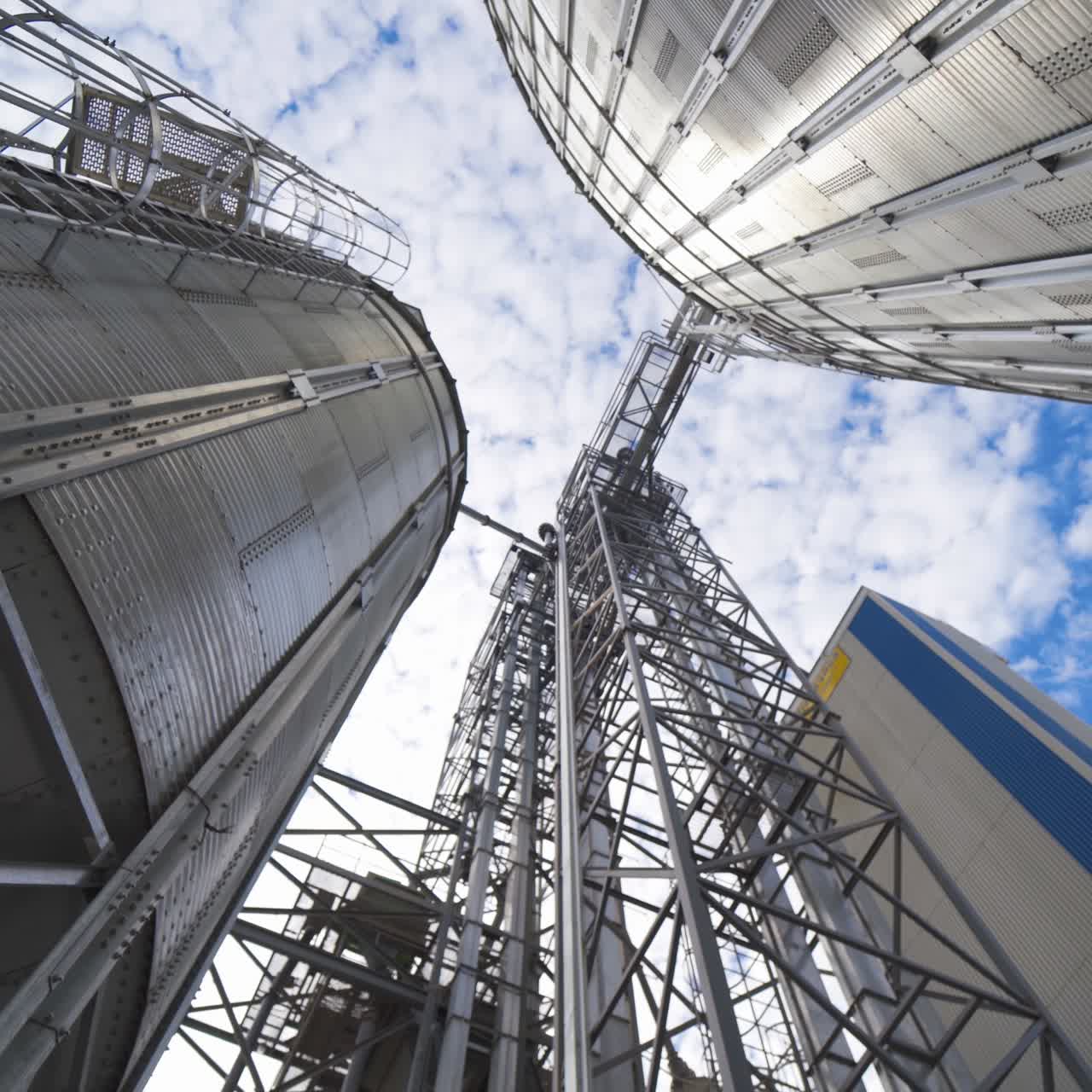 Metal construction of a modern agricultural factory. Industrial plant for storage and processing seeds. Grain elevators outdoors. View from below