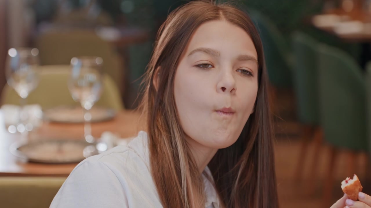 Giovane donna che assaggia un dolce al ristorante con espressione pensierosa, tavolo elegante con bicchieri e sedie verdi, masticazione lenta e sottile delusione, luce calda cinematografica, ritratto ravvicinato di una giovane cliente.