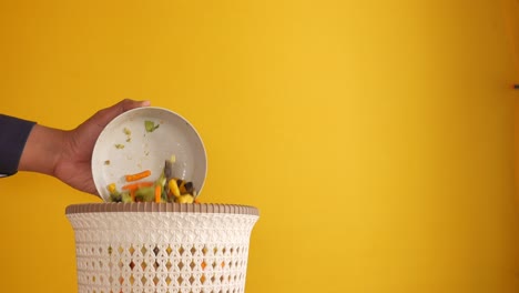 tirando verduras en un cubo de basura