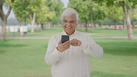 Indian-old-man-scrolling-through-phone-in-park