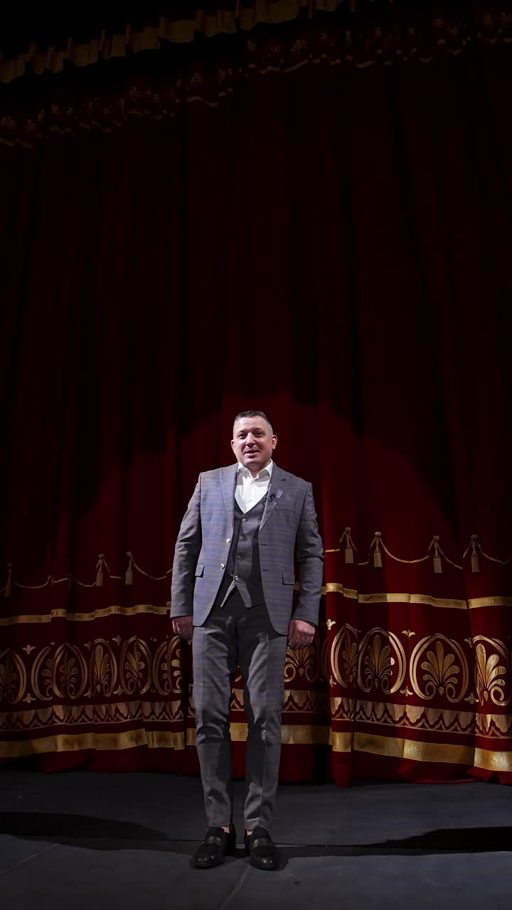Male host talking on stage. Elegant man in grey costume performing on large scene uses gestures. Actor moving joyfully on stage. Vertical video