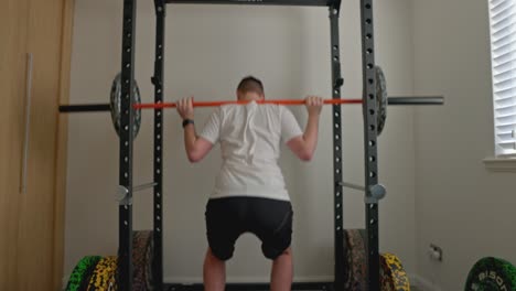 static shot of a young man squatting a barbell with extra plates in a squat rack