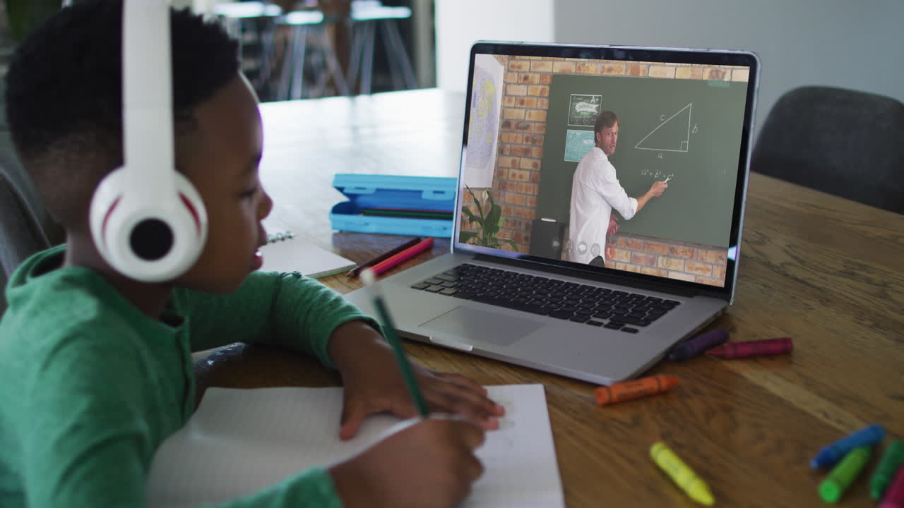 African american boy sitting at desk using laptop having online school lesson