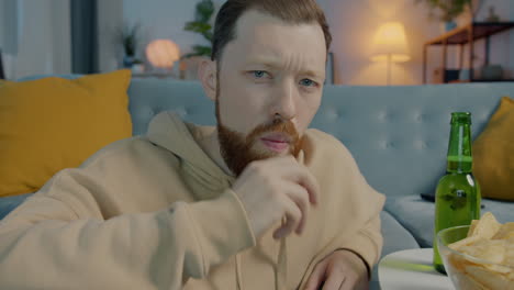 man watching tv, drinking beer and eating chips