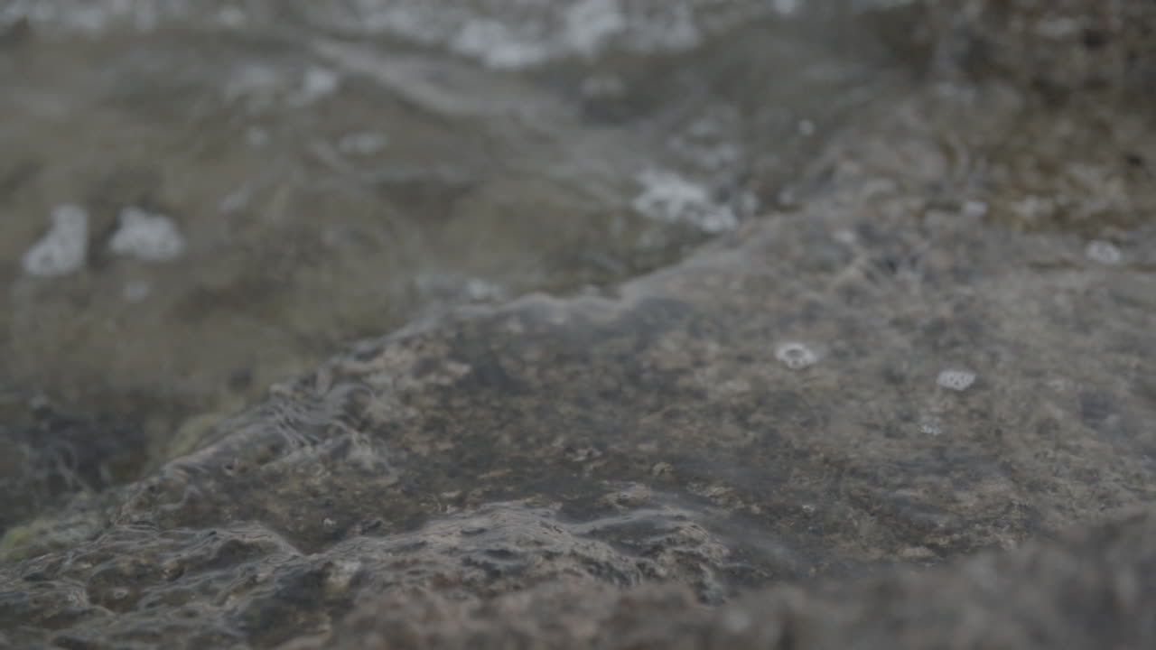 Primo piano al rallentatore dell'acqua che colpisce le rocce vicino alla riva e schizza.