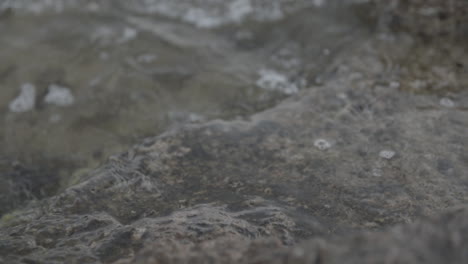 close up slowmotion shot of water hitting some rocks near the shore and splashing log