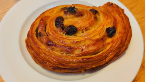 pain au raisin french pastry dessert snack on white plate in natural lighting.