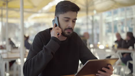 joven serio hablando por teléfono inteligente y usando una tableta