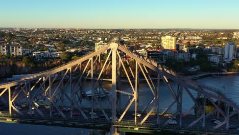 Un-Dron-Aéreo-Cinematográfico-Vuela-Alrededor-Del-Histórico-Puente-De-La-Historia-De-Brisbane-Que-Captura-El-Tráfico-De-Vehículos-Ocupados-Que-Cruza-El-Río-Entre-Kangaroo-Point-Y-Fortitude-Valley-Y-Personas-En-La-Escalada-De-Aventuras-Al-Atardecer.