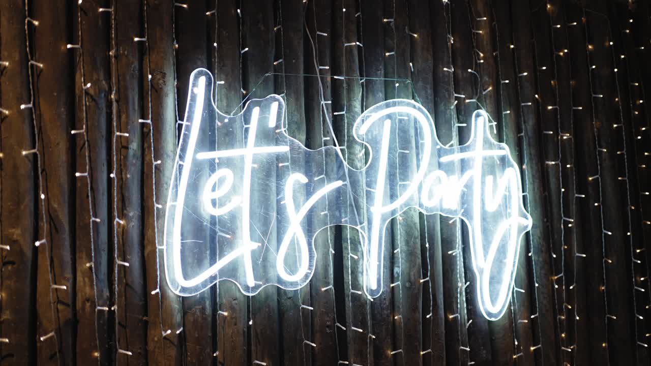 Glowing neon "Let's Party" sign on rustic wood with fairy lights