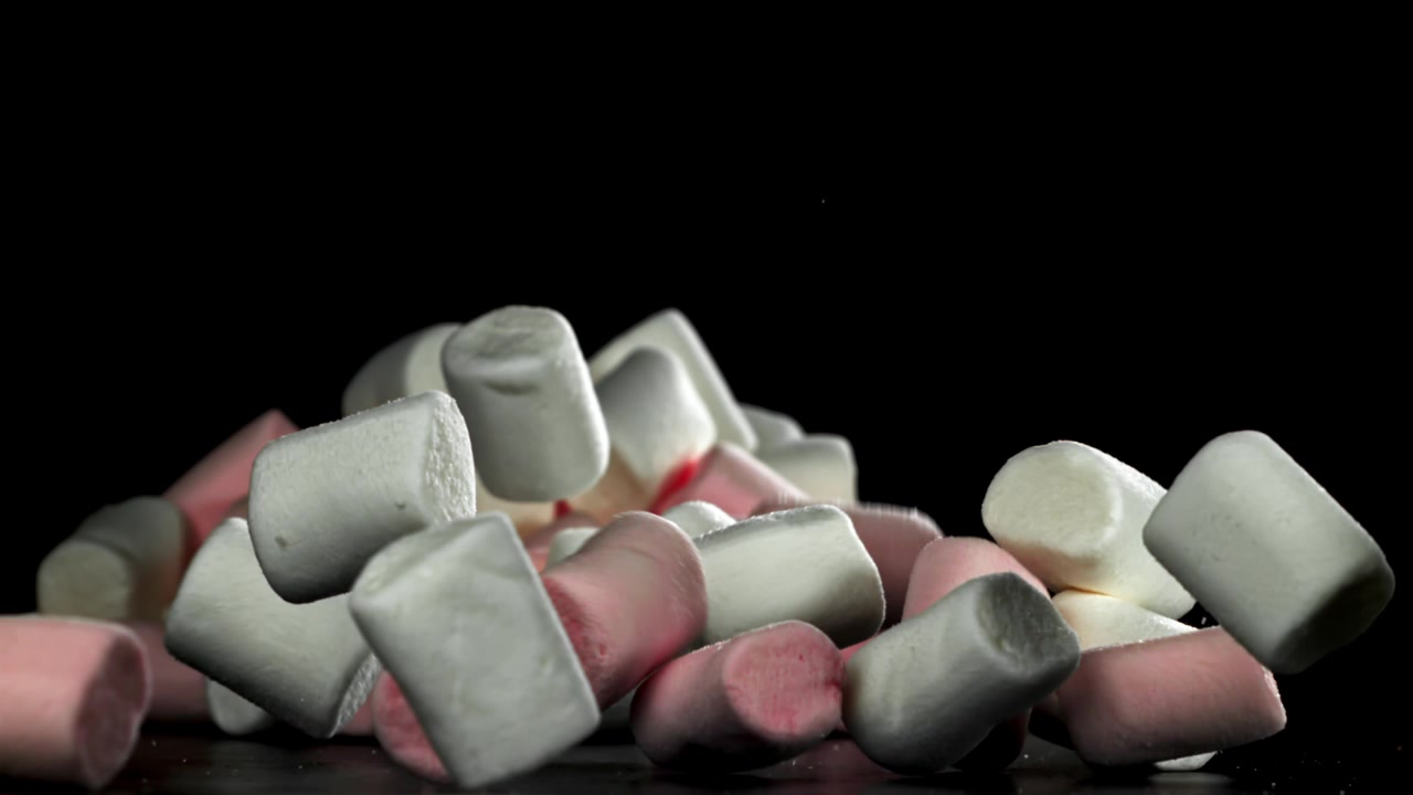 Marshmallow rosa e bianchi che cadono e si accumulano su sfondo nero