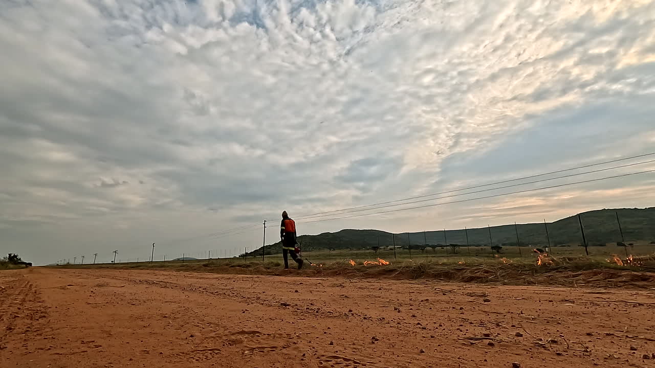 Low-angle of firefighter managing wildfire along African wilderness fence line