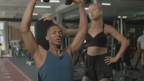 una vista de cerca de una mujer caucásica y un atlético afroamericano en el gimnasio.
