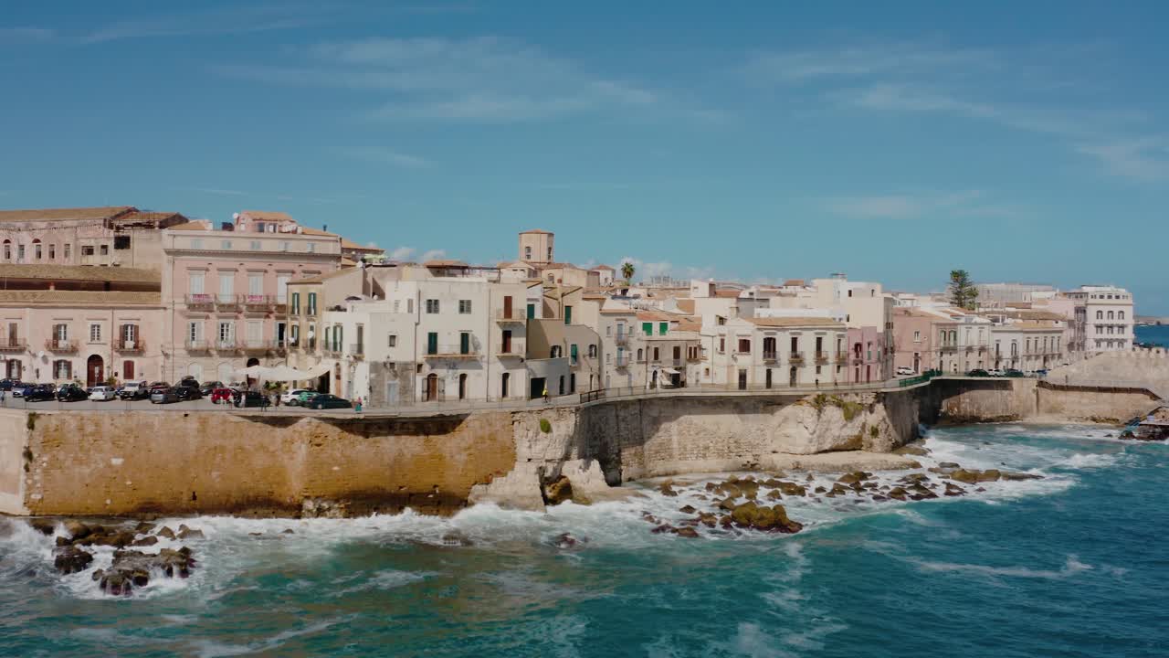 Aerial orbit drone shot of Ortigia island by Mediterranean sea with waves crashing at the fortress wall. Historic town in Sicily.