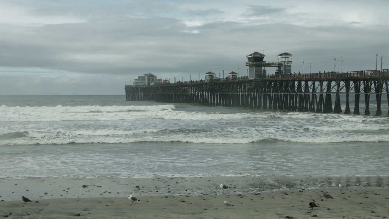 UHD footage of Oceanside Pier and beach on a cloudy morning, with soft waves, moody skies, and tranquil coastal vibes—perfect for travel, tourism, nature, and atmospheric seaside scenes.