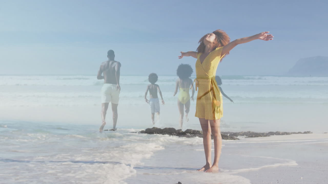 On beach, woman in yellow dress with family running, enjoying animation