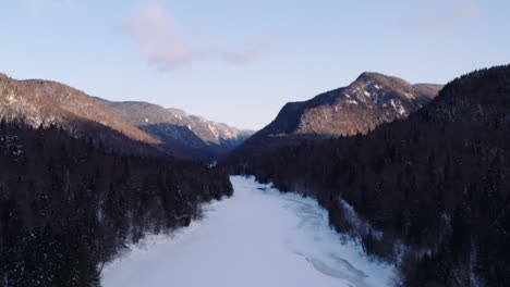 Grúa-Aérea-épica-Hasta-El-Río-Nevado-De-Movimiento-Vertical-Que-Fluye-Del-Fiordo-En-El-Bosque-Boreal-De-Invierno,-Parque-Nacional-De-La-Jacques-Cartier,-Quebec,-Canadá