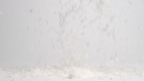 white coconut flakes raining down onto white tabletop and landing in a pile in slow motion