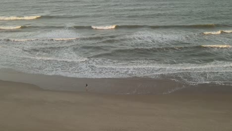 Aerial-drone-orbiting-around-isolated-person-walking-on-beach-at-sunset,-Playa-La-Viuda-in-Uruguay