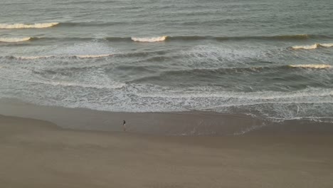 drone aéreo orbitando alrededor de una persona aislada caminando en la playa al atardecer, playa la viuda en uruguay
