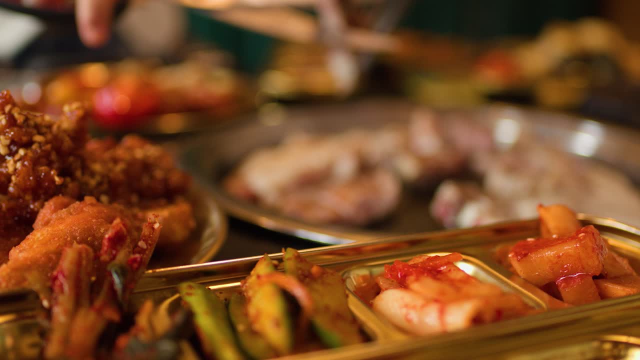 Hand cuts grilled meat with scissors, surrounded by Korean side dishes under warm indoor lighting