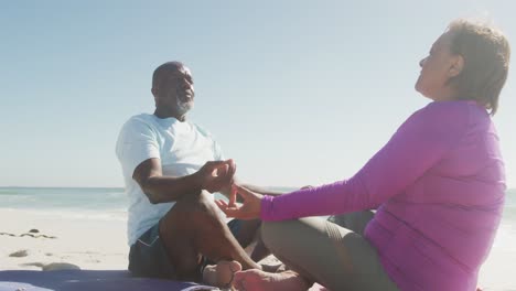 senior african american couple practicing yoga and meditating on sunny beach