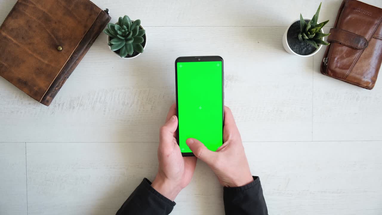 teléfono con pantalla verde en la mesa con portátil y bolso vista desde arriba, teléfono inteligente chromakey espacio de copia de pantalla