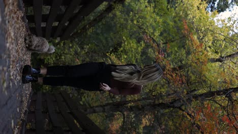 blonde woman walking with adorable puppy outside in autumn forest, vertical