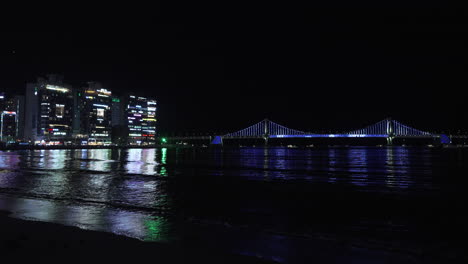 illuminated gwangan bridge changing light colors - seafront view from night gwangalli beach