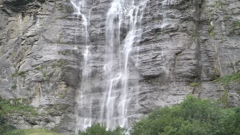 giant waterfall over the rocks falling down on a bright day in lauterbrunnen in switzerland between the green trees. slowmo shot