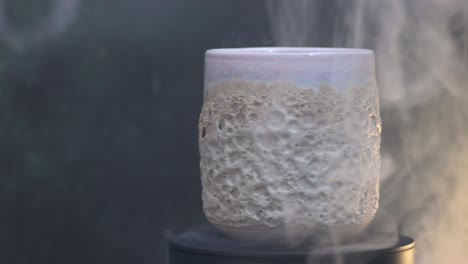 dolly a la izquierda de un vidrio de cerámica con textura de coral girando alrededor de su eje en el humo amarillo