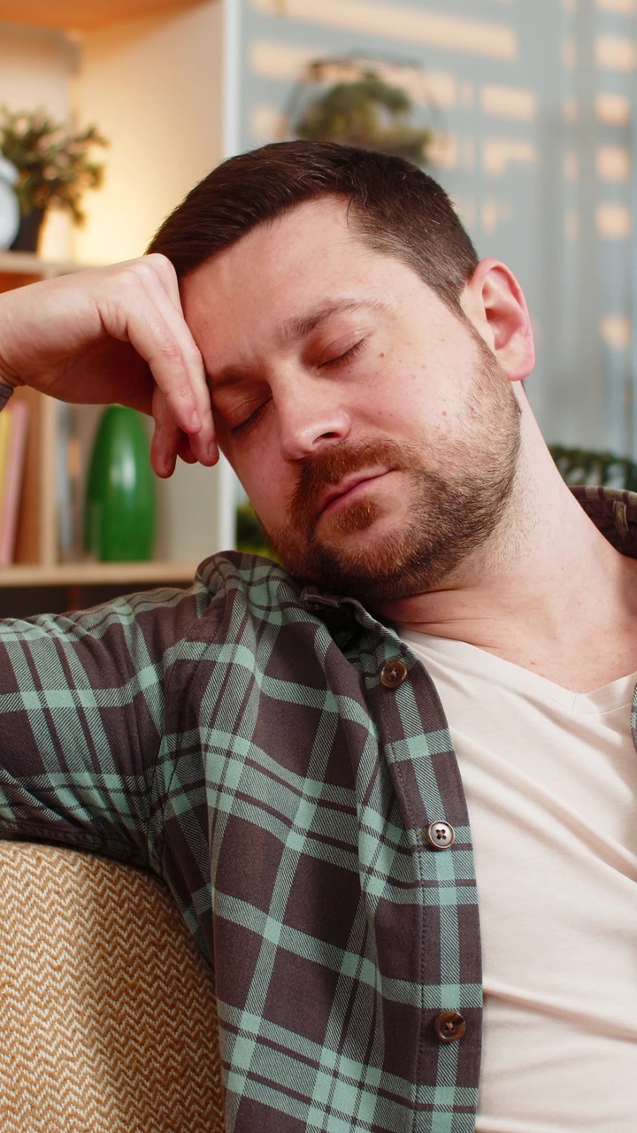 Giovane uomo sul divano di casa che si addormenta per la stanchezza dopo lo stress di un lavoro estenuante e il burnout serale.