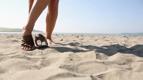 Frau-Zieht-Sandalen-Am-Strand-An