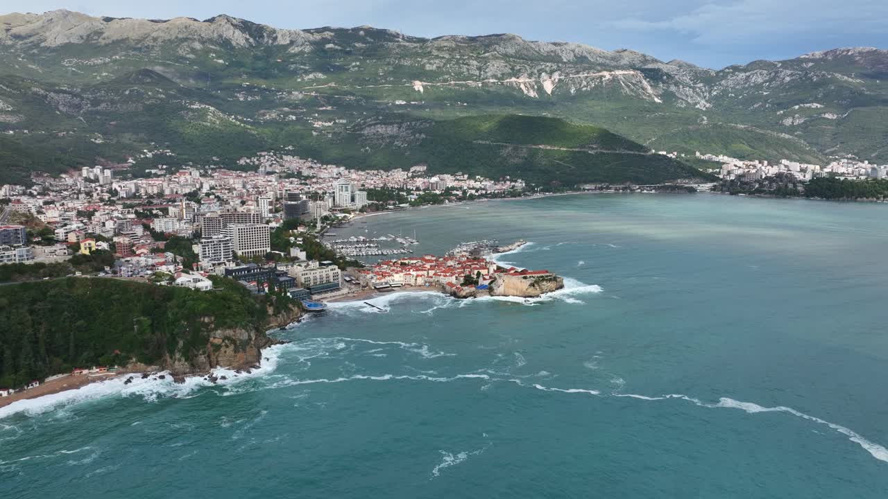 Drone panoramic revealing orbit of Budva peninsula surrounded by bright turquoise sea and red roofs