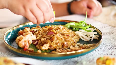 las manos adornando pad thai con lima y brotes