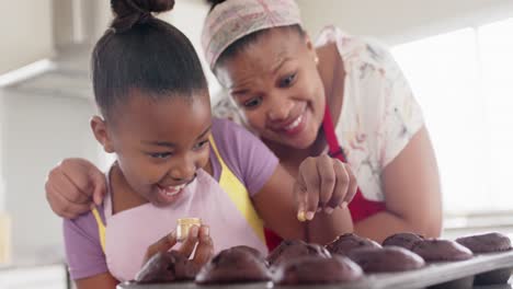 Happy-unaltered-african-american-mother-and-daughter-baking,-decorating-cupcakes,-in-slow-motion