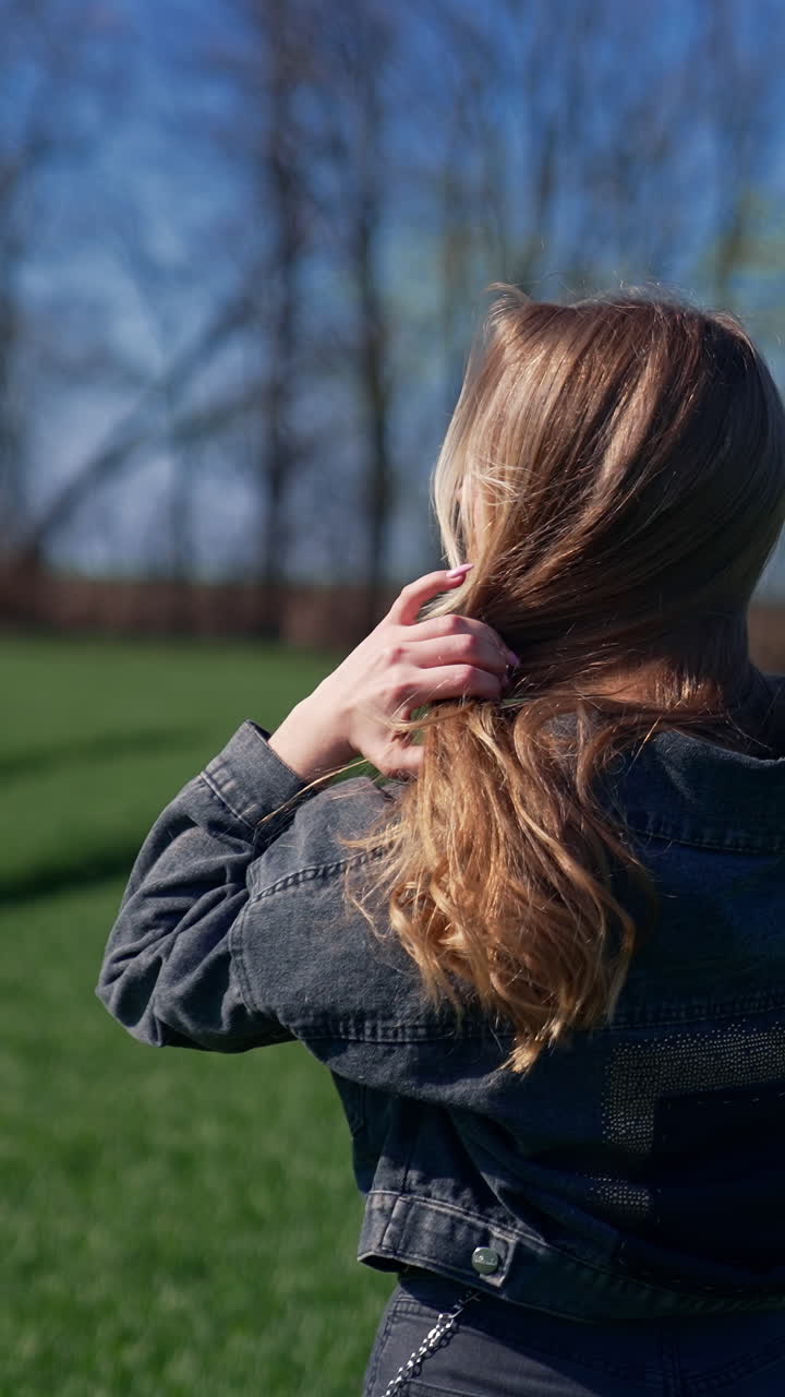 Beautiful girl in the countryside. Attractive young model with long blond hair posing on camera on the field. Orbital view. Vertical video