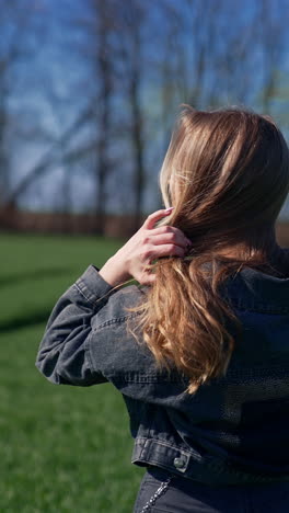 beautiful girl in the countryside. attractive young model with long blond hair posing on camera on the field. orbital view. vertical video