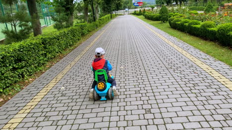 energetic caucasian toddler riding quickly his toy car outdoors. kid stops and beeps his horn cheerfully.