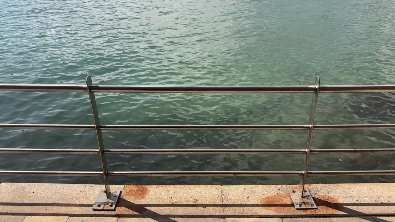 barandilla de metal junto a las tranquilas aguas color turquesa de la playa de Porto Cristo en Mallorca bajo una cálida luz solar