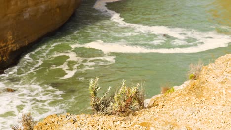 waves gently crash against the rocky cliffs of loch ard gorge under bright sunlight, showcasing the natural beauty of port campbell