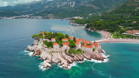 sveti stefan, montenegro. aerial drone view of famous and luxury travel destination. static footage. tourist boat passing. at right sveti stefan beach.