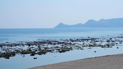 Scenic-Timorese-view-of-Cristo-Rei-statue-and-ocean-at-low-tide-with-hazy-light-in-capital-city-of-Dili,-Timor-Leste,-Southeast-Asia